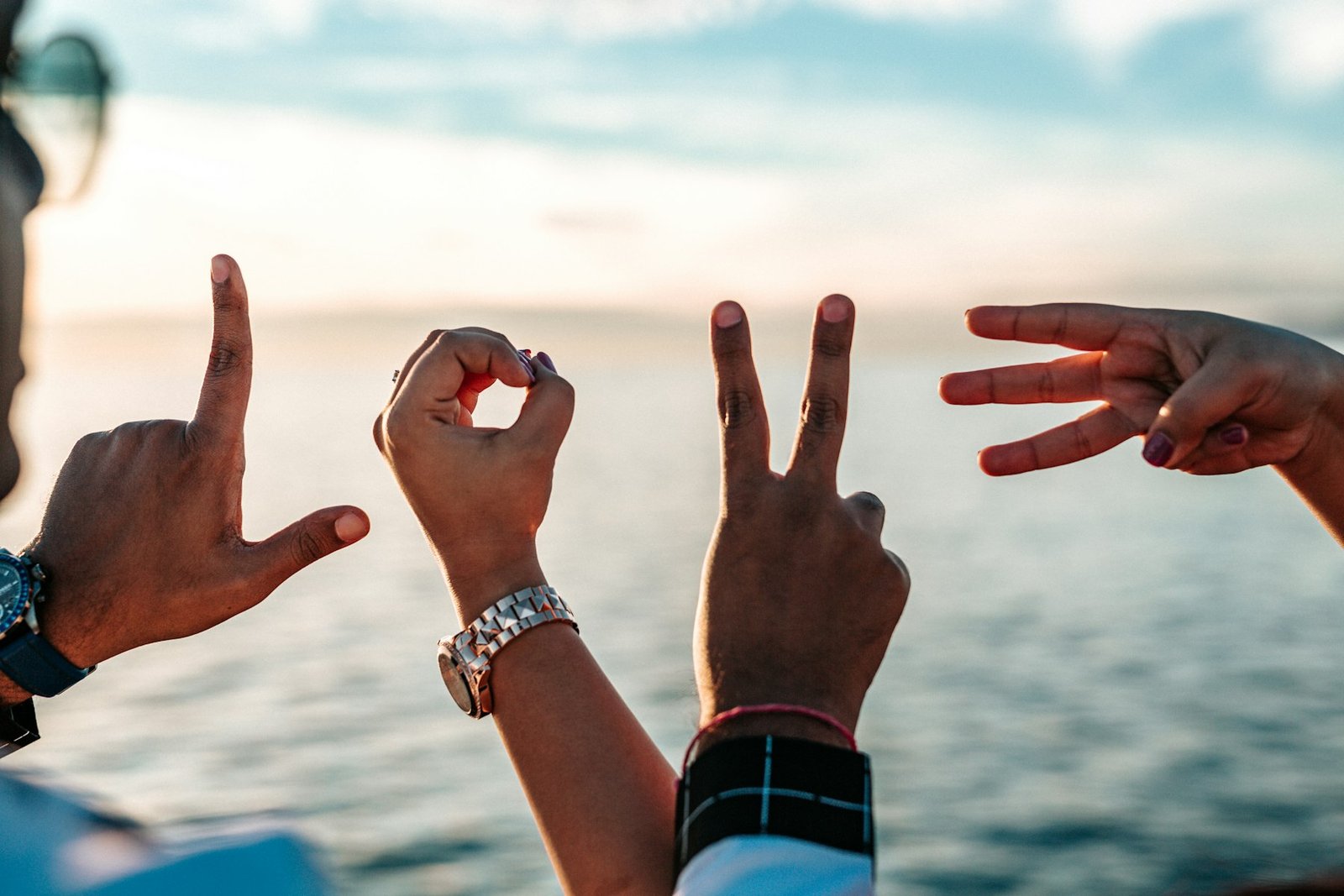 Guests' hands spelling out LOVE against an ocean sunset