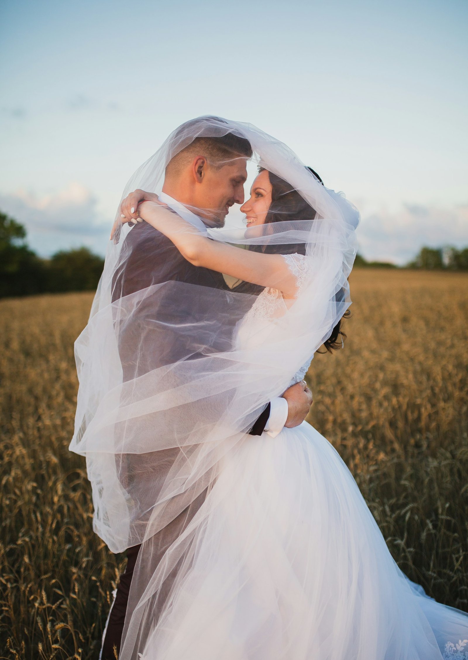 Couple embracing under a bridal veil in a golden wheat field
