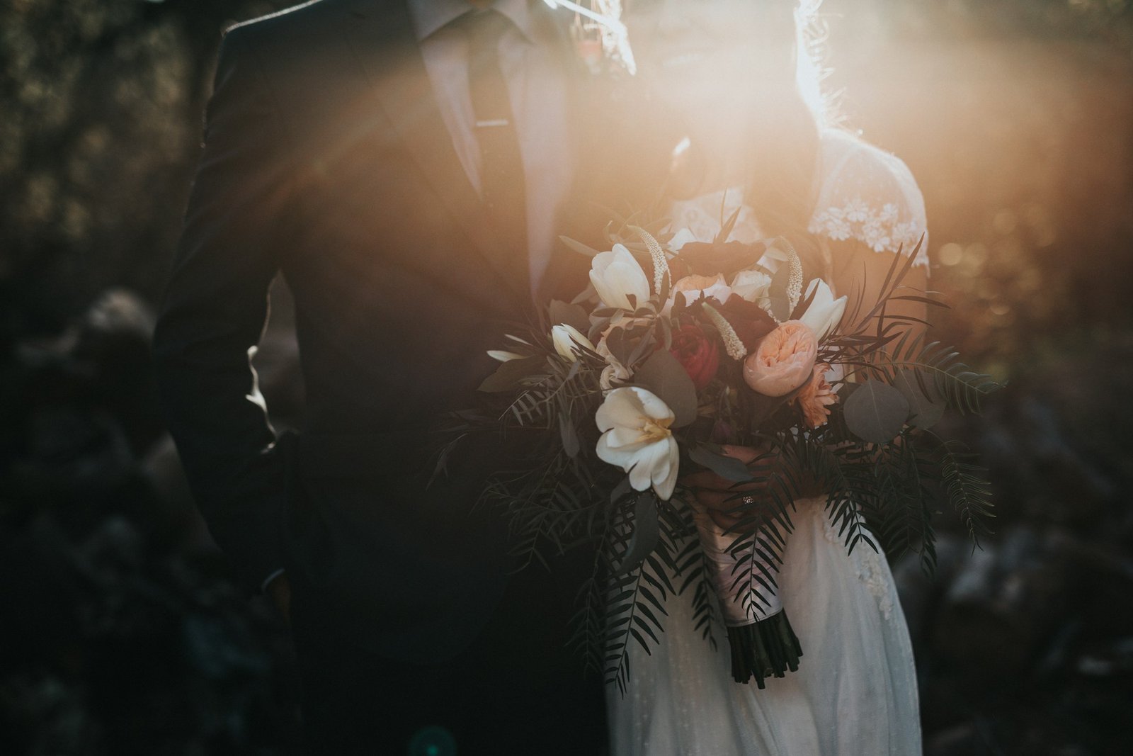 Backlit wedding bouquet held between bride and groom